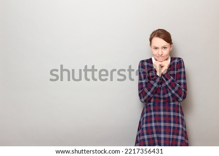 Studio portrait of anxious young woman looking disappointed and confused, being worried about mistakes made, with  clenched hands under her head, standing over gray background, with copy space