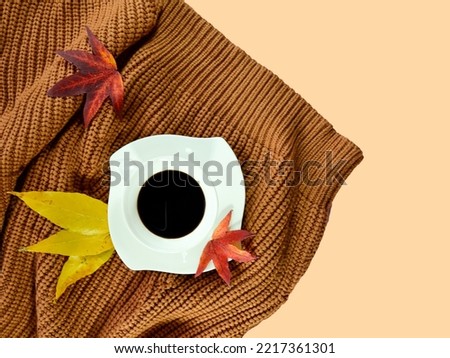 Creative autumn design made of white coffee mug with camel sweater and red leaves against pastel yellow background. Minimal concept. Copy space. Fall art. Autumn coffee. Girl essentials.