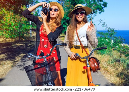 Outdoor fashion lifestyle portrait of two pretty smiling peat friends girls, walking near sea side have perfect  free vacation day together, taking pictures an retro camera, wearing vintage clothes.