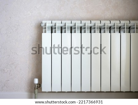 Heating radiator on light wall background, white metal water heater in home room. Concept of warmth, energy crisis, saving, contemporary radiator.