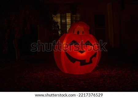 Glowing night Halloween house outdoor decoration. Inflatable pumpkin near the house