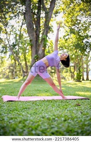 Portrait, Healthy millennial Asian woman in sportswear exercising in the green nature garden, practicing triangle forward yoga pose.