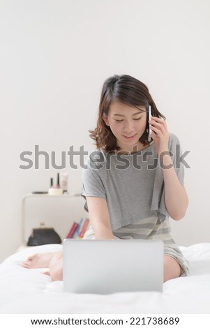 Young Asian woman using laptop computer on a bed.