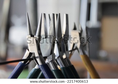 Round nose pliers, flat pliers and other jewelry making tools for cutting and bending wire at the jewellers bench in a professional jewellery workshop. Steel equipment with colorful handles. Royalty-Free Stock Photo #2217400613