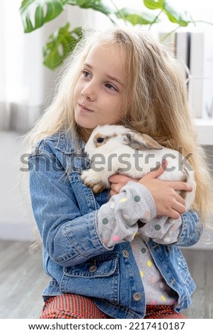 Caucasian child hold rabbit in arms, Children play with real rabbit. Laughing child at Easter egg hunt with white pet bunny. Little toddler girl playing with animal. Summer fun for kids with pets.