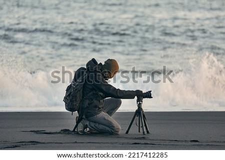 Photographer on an Icelandic black sand beach coastline, huge waves in the background