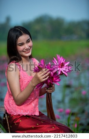 Enjoying happy beautiful young Thai woman farmers working posting playing smiling in the lotus farm and holding the lotus flowers in the lotus lake countryside view