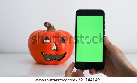 Use green screen for copy space close up. Chroma key mock-up on smartphone in hand. Woman holds mobile phone and clicking on screen. Pumpkin on the background