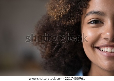 Closeup cropped front half face view of beautiful African teenage girl having natural afro curly hairs and charming wide toothy smile looks at camera. Advertises dental clinic services, gen Z person Royalty-Free Stock Photo #2217455961