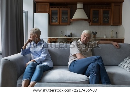 Older silent couple after quarrel sit on sofa apart, not talking, feeling annoyance, looking frustrated due to misunderstanding, lack of understanding between spouses. Family conflict, marital crisis Royalty-Free Stock Photo #2217455989