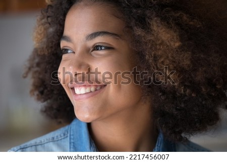 Portrait of beautiful African teen age girl staring aside feeling happy. Close up smiley face of adolescent looking into distance, having white-toothed smile, positive face expression and perfect skin