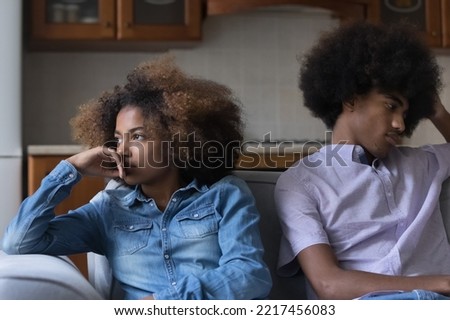 Sad silent African teenagers sit on sofa at home separately after quarrel. Young pensive couple thinks over troubles in relations, having difficulties in relationships. First love, quarrels, jealousy Royalty-Free Stock Photo #2217456083