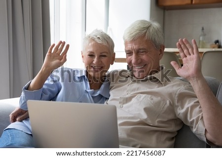 Attractive older wife and husband greeting friend or grown up children use video call app, staring at laptop screen smile start distancing communication feel happy. Modern tech, virtual meeting event Royalty-Free Stock Photo #2217456087