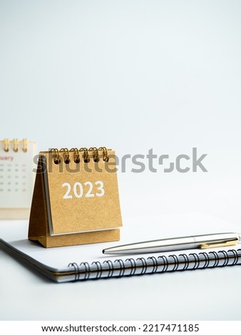 Happy new year 2023 background. 2023 numbers year on small beige desk calendar cover on notepad with pen on white background with copy space, vertical style.