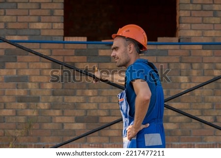 a man in a construction helmet and overalls is resting at a construction site, building a house. High quality photo