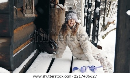 winter portrait. cutie, pretty little girl, dressed in warm winter clothes, fully covered with snowflakes, sitting on a bench by an old wooden house. happy time on snowy winter day. High quality photo