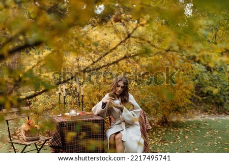 Picnic in nature in the garden. Girl in warm clothes sits at a table with a cup in her hands