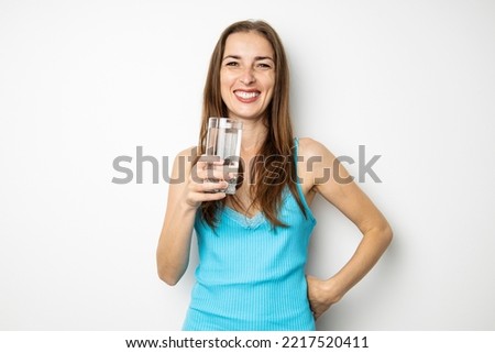 Smiling young woman holding glass of water on white background.