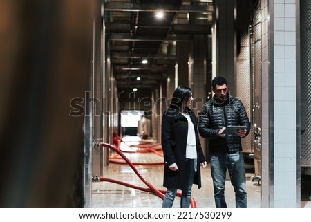 Caucasian couple during the winery visit, walking through the production industry cellar using a tablet to know the process of the winemaking Royalty-Free Stock Photo #2217530299