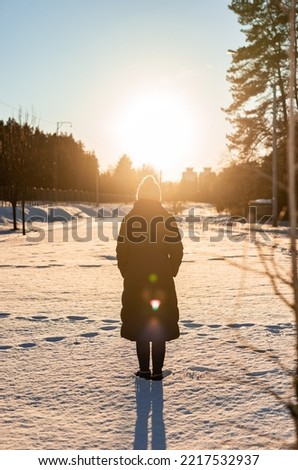 Back view of woman standing in snow and looking at sun light. Peaceful winter atmosphere. Spending time alone. High quality photo