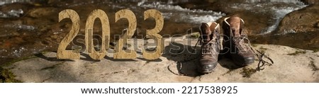 Rocky 2023 on a mountain riverside with a pair of trekking shoes ready for adventure. Active new year concept. Royalty-Free Stock Photo #2217538925