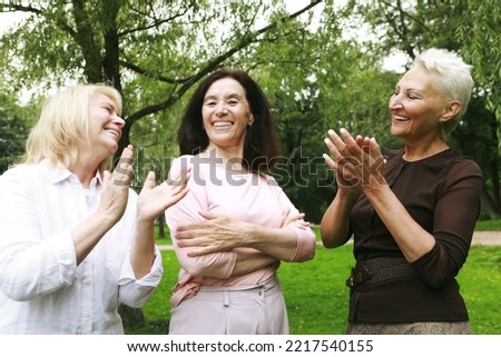 Women friends in the park celebrate a birthday. Clap your hands, congratulate, rejoice. Happy summer day. The concept of friendship, happy old age and emotions.