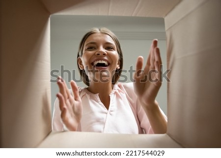 Happy laughing young woman putting arms into box, feeling excited receiving order from internet store. Joyful female customer satisfied with fast delivery service, getting parcel, shipping concept. Royalty-Free Stock Photo #2217544029