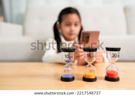 The sandclock with difference time in the background of little girl playing the smartphone. Concept of kid and technology and impact child development. Royalty-Free Stock Photo #2217548737