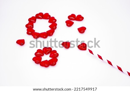 Red glass hearts are stacked in a circles like a soap bubbles, or lollopop with a paper striped cocktail straw. Copy space