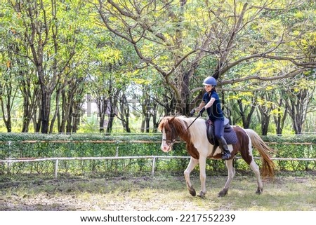 Portrait of smiling female jockey riding horse. Caucasian woman and horse training in the afternoon.