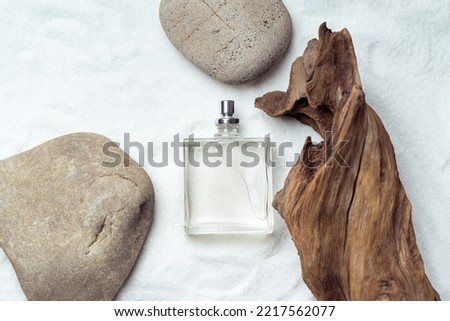 Perfumery. Transparent perfume bottle on a sand near the weathered wooden snag and stones. Top view. Royalty-Free Stock Photo #2217562077
