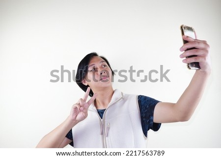 Portrait of an attractive young man taking a selfie while standing and giving peace sign finger isolated over white background