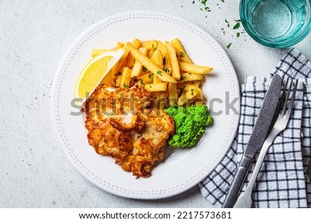 Fish and chips. Cod fish in batter with french fries and mashed green peas on white plate, gray background, copy space, top view. English food concept. Royalty-Free Stock Photo #2217573681