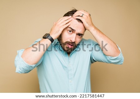 Worried caucasian man looking at his receding hair and stressed about hair loss or baldness Royalty-Free Stock Photo #2217581447