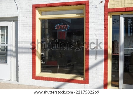 Large colorful store front window with a neon open sign and a red painted border