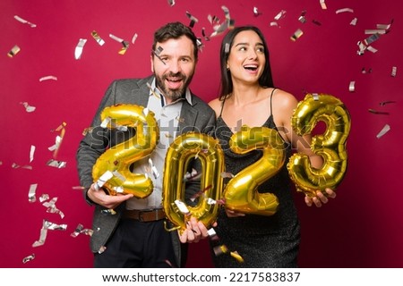 Beautiful couple looking excited celebrating new year's eve 2023 with balloons and confetti Royalty-Free Stock Photo #2217583837