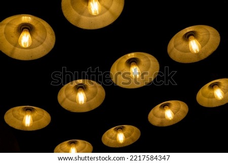 Hanging line of antique and vintage lamps. Series of old light bulbs in warm orange yellow color temperature on a ceiling. Old and dusty lamp shade. Pattern of glowing old-fashion hanging lamp.