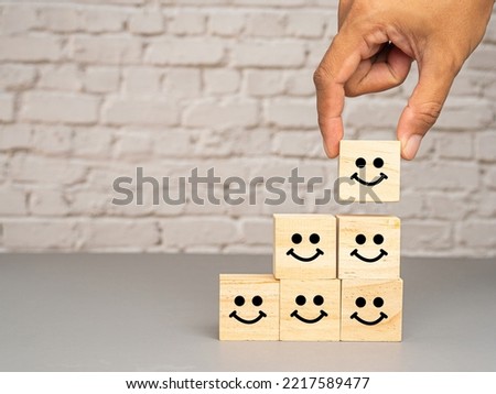 Satisfaction concept. Side view of wooden cubes with stacked smile icons over a table with white brick wall background. Happy mood icons. Feedback emotion scale Royalty-Free Stock Photo #2217589477
