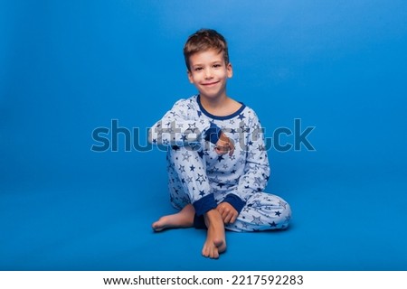 a little boy is sitting in pajamas on a blue background. the concept of healthy sleep. pajamas made of natural material for children