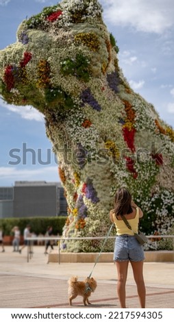 A young happy caucasian woman taking a photo in front of the Puppy sculpture in Bilbao