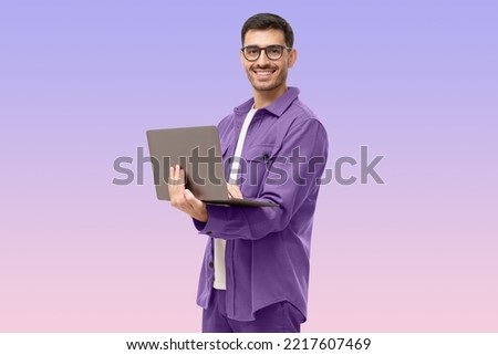 Young man standing holding laptop and looking at camera with happy smile, isolated on purple background Royalty-Free Stock Photo #2217607469
