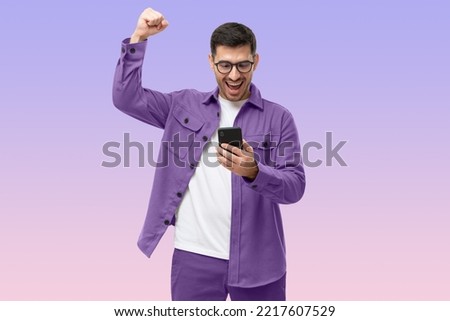 We've got a winner! Happy young man in purple shirt looking at phone screen with victory expression, isolated on purple gradient background