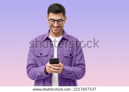 Young man looking at phone, standing isolated on purple background