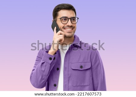 Portrait of handsome young man in purple shirt and glasses, answering phone call, looking aside with smile, isolated on purple background Royalty-Free Stock Photo #2217607573