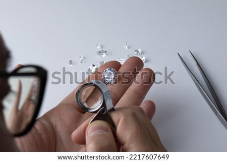A diamond dealer participating in an international jewellery exhibition evaluates the quality and color of diamonds using a magnifying glass. Royalty-Free Stock Photo #2217607649
