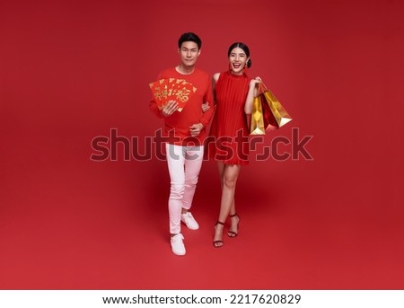 Happy Asian couple holding shopping bags and red envelopes isolated on red background for Chinese new year shopping concept. Royalty-Free Stock Photo #2217620829