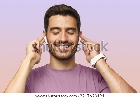 Close up shot of smiling young man in purple t-shirt listening his favourite song or cool track, feeling the rhythm and vibe with eyes closed