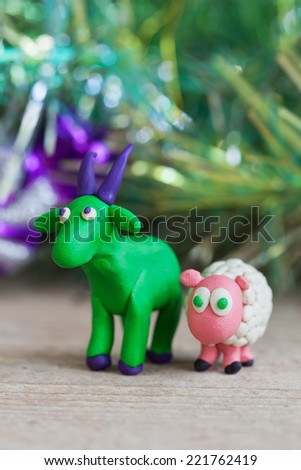 Plasticine world - little homemade green goat with purple horns and hooves and sheep stands on a wooden floor, selective focus and place for text