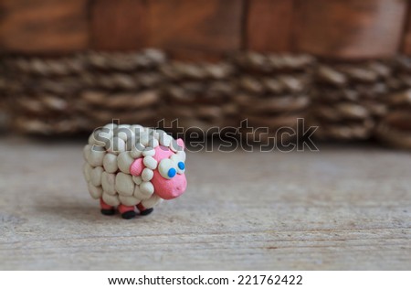 Plasticine world - little homemade white sheep with blue eyes stand on a wooden floor, selective focus and place for text