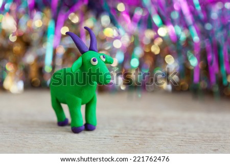 Plasticine world - little homemade green goat with purple horns and hooves stand on a wooden floor, selective focus and place for text